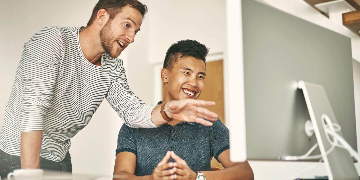 Two coworkers collaborating on sb 553 compliance strategies at a computer, discussing workplace violence prevention measures.