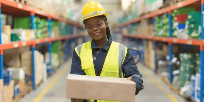 Woman wearing hardhat and safety vest holding a box representing cpg industry risks