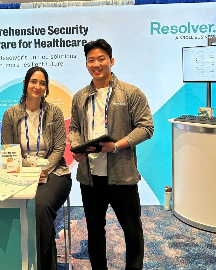 Exploring community & innovation at iahss 2024 2 Two people, a woman and a man, are posing at a booth for resolver's healthcare security software at the iahss 2024 conference. The backdrop highlights the software's key features, and the display includes a section labeled "common challenges faced in hospitals," focusing on issues like vulnerable patients, security regulations, and workplace violence.