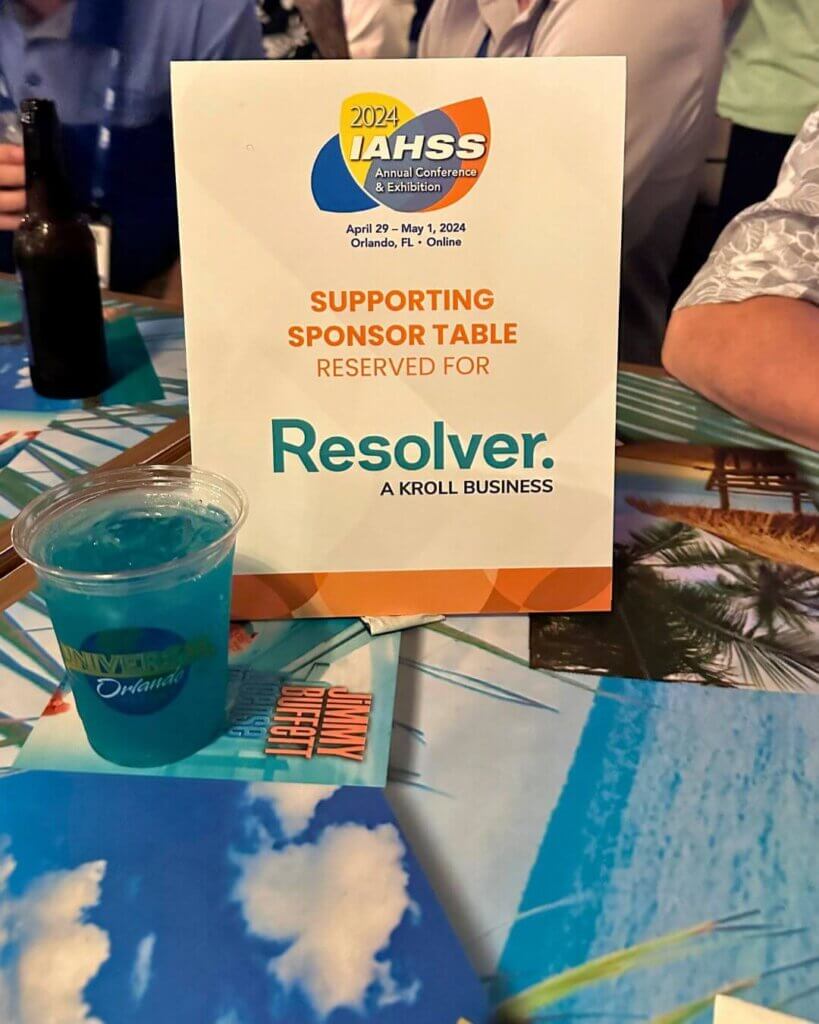 Exploring community & innovation at iahss 2024 4 A close-up shot of a supporting sponsor table reserved for resolver at the iahss 2024 conference in orlando, florida. The table includes a colorful sign with the iahss logo and a blue drink with a universal studios orlando logo on the cup, creating a fun and branded atmosphere.