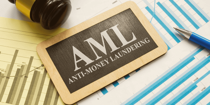 An overhead view of a work desk featuring a small wooden plaque with "aml anti-money laundering" inscribed on it, a judge's gavel, a pen, and financial line graphs printed on paper representing eu anti-money laundering authority