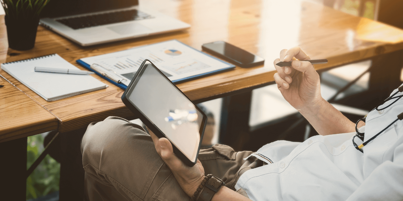 A professional conducting a vendor risk assessment on a digital tablet, with a notepad, smartphone, and financial reports on the desk.
